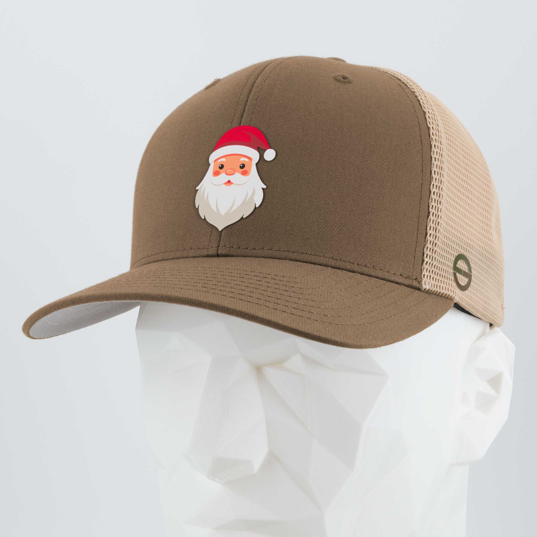 The Eternal Glyph Santa Hat (Silicone) Flexfit® Mesh Trucker Cap in coyote/khaki sits on a white geometric mannequin head, featuring a cartoon Santa Claus with a red hat on the front.