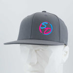 A Dark Gray Flexfit® Flat Bill Premium Fitted Cap from Eternal Glyph, featuring a blue and pink SD silicone logo on the front, is showcased on a white geometric mannequin head against a light background—an ideal choice for dedicated members of the Staying Driven online fitness crew.