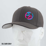 A dark gray Eternal Glyph Staying Driven (Silicone) Flexfit® Premium Wool Blend Cap, featuring a pink and blue SD logo on the front, is displayed on a white geometric mannequin head. Premium headwear crafted for the online fitness community. Text in the lower left corner reads XXL DARK GRAY.