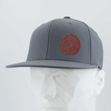 The Eternal Glyph Moab Spiral Petroglyph (Silicone) Flexfit® Flat Bill Premium Fitted Cap is a gray snapback hat with a red spiral petroglyph design on the front, shown on a white geometric mannequin against a light background.
