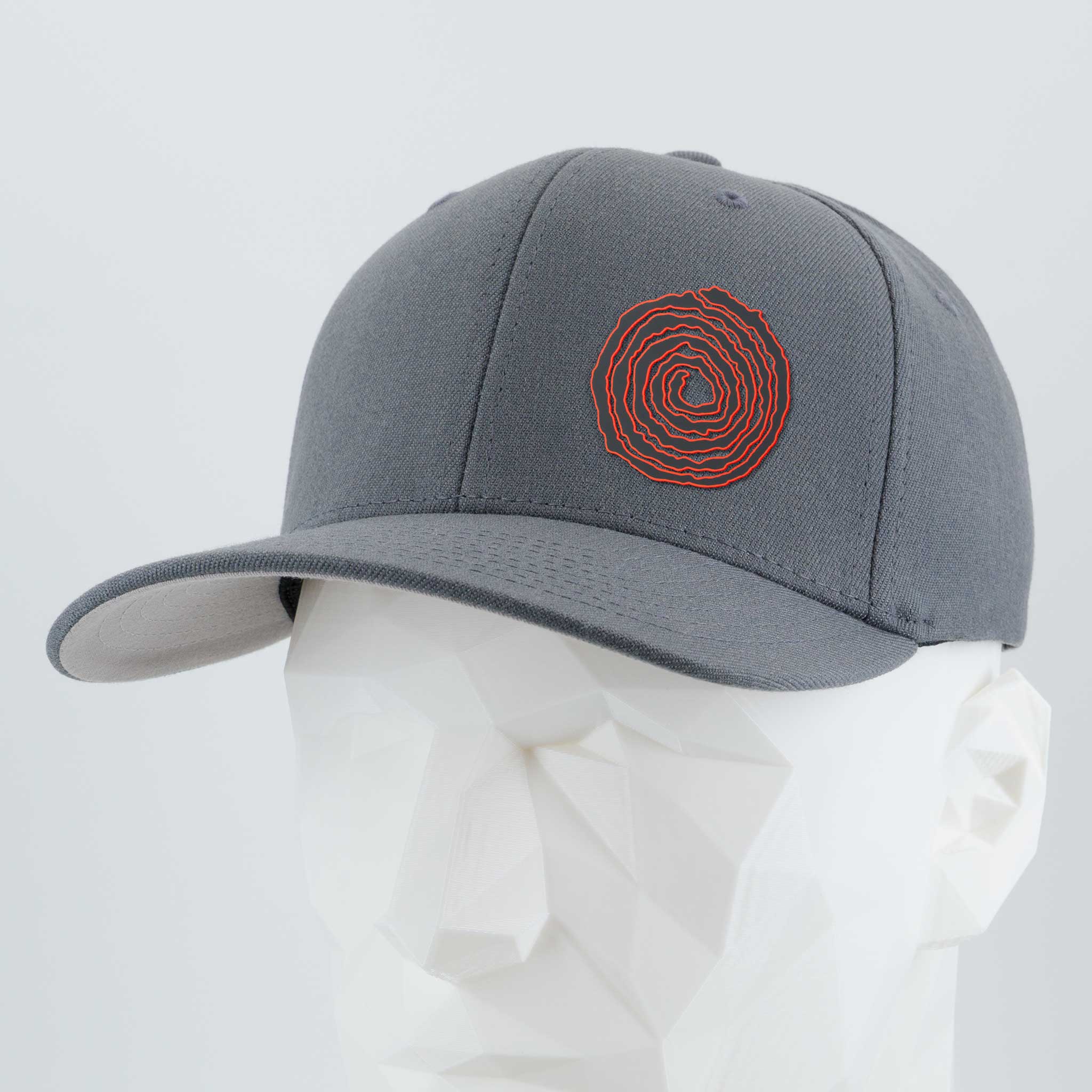 The Eternal Glyph Moab Spiral Petroglyph (Silicone) Flexfit® Premium Wool Blend Cap in dark gray features a red ancient-inspired spiral design on the front, shown on a white geometric mannequin head against a plain light background.