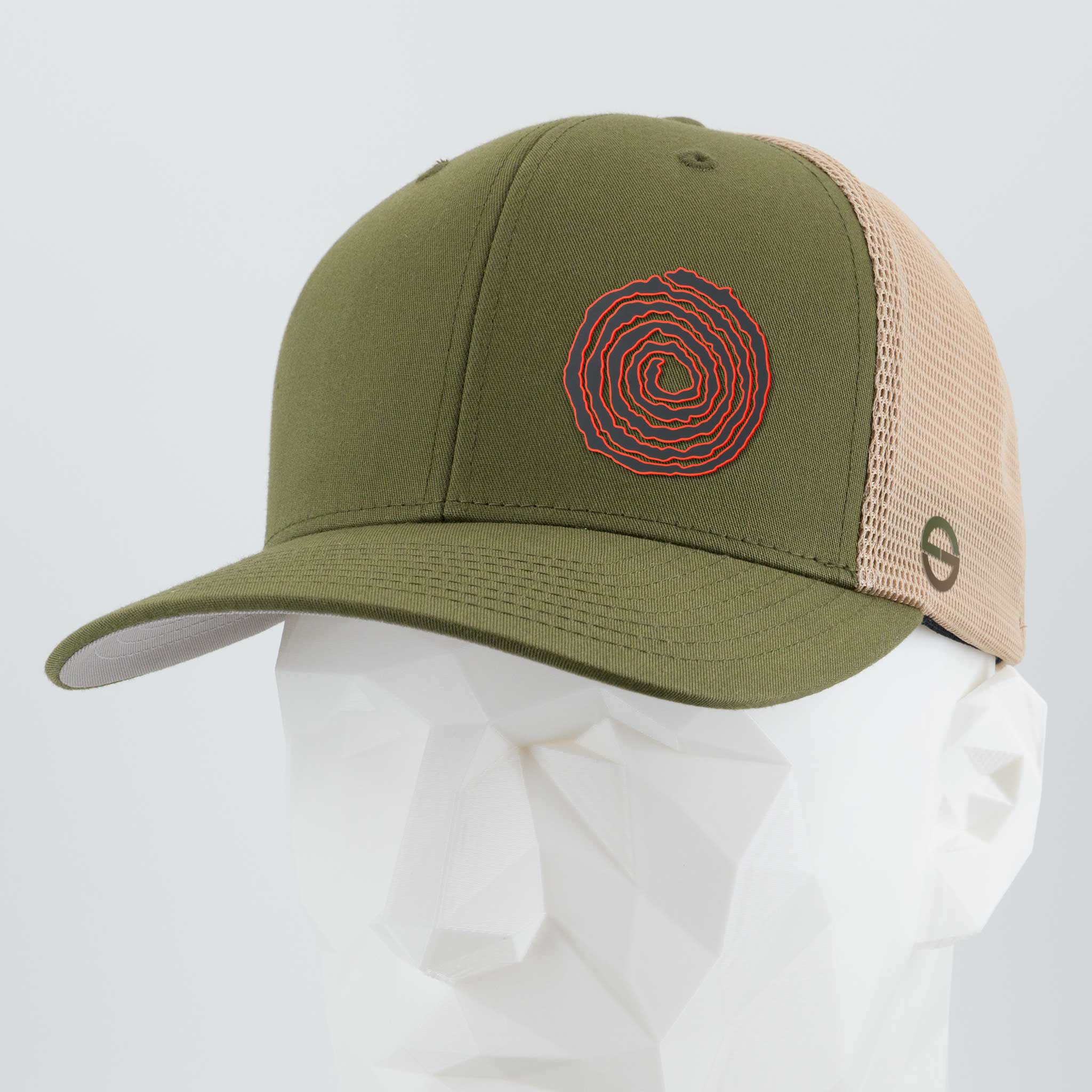 The Eternal Glyph Moab Spiral Petroglyph (Silicone) Flexfit® Mesh Trucker Cap in olive green and beige features a red and orange ancient symbol-inspired design, shown on a white geometric mannequin head.