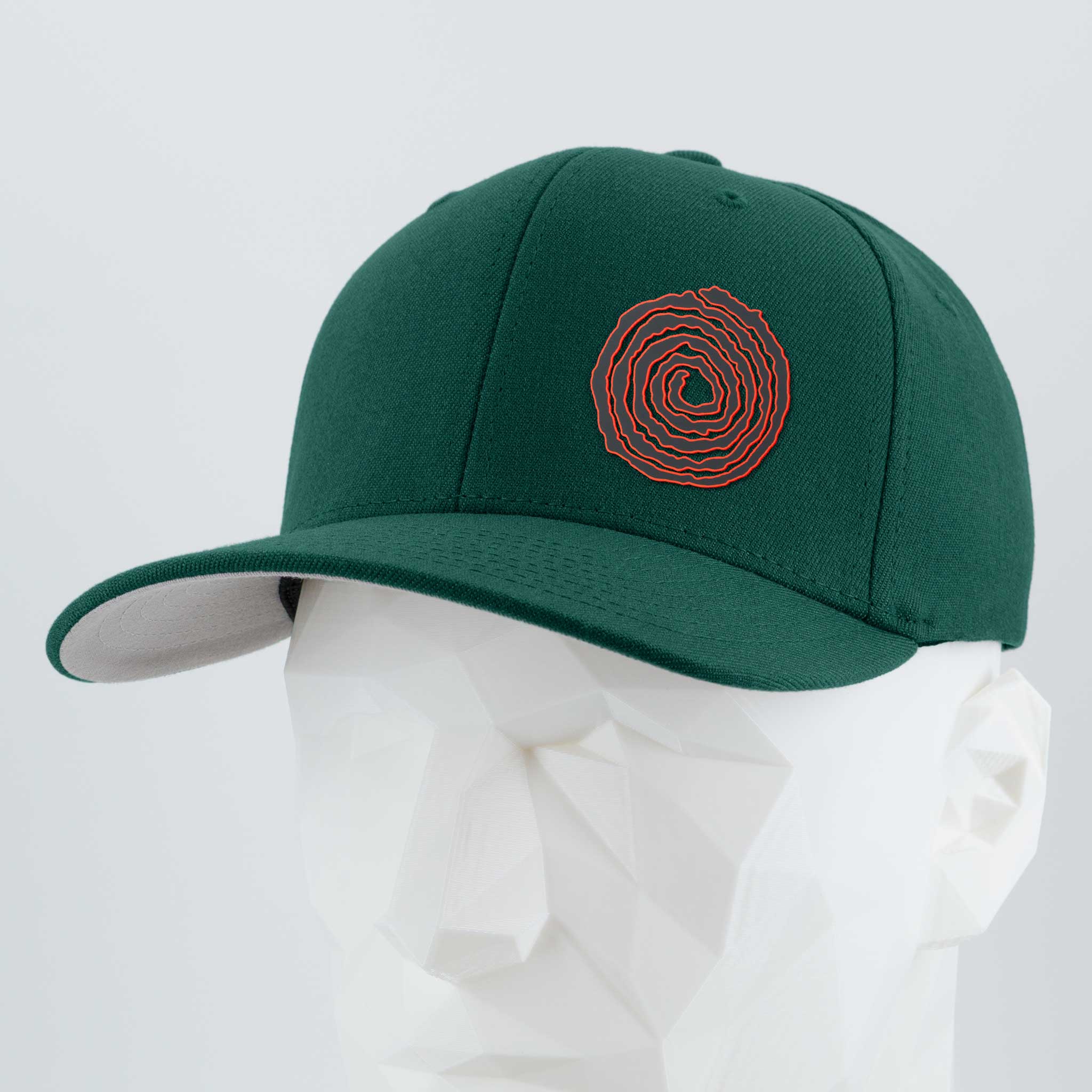The Eternal Glyph Moab Spiral Petroglyph Flexfit® Premium Wool Blend Cap in Spruce features a red spiral inspired by ancient rock art, shown on a white geometric mannequin head against a light gray background.