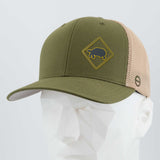 The Eternal Glyph Tortoise Crossing Sign (Silicone) Flexfit® Mesh Trucker Cap in olive green and beige sits on a white geometric mannequin, featuring a yellow tortoise road sign patch symbolizing patience and resilience.