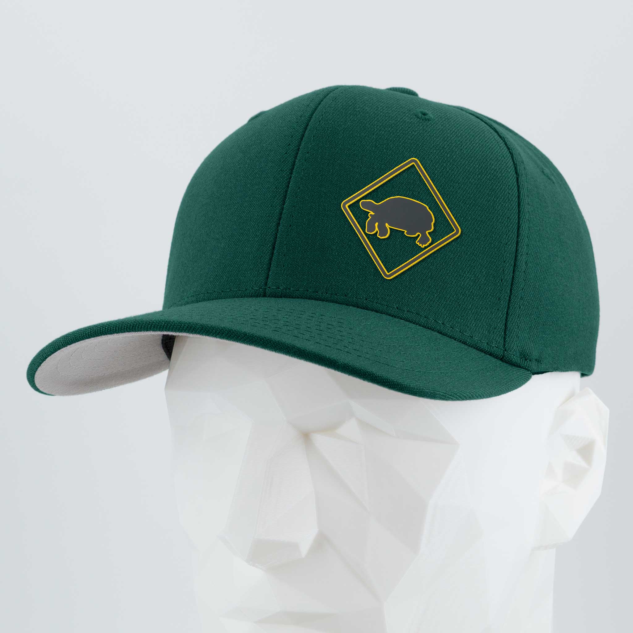 The Eternal Glyph Tortoise Crossing Sign (Silicone) Flexfit® Premium Wool Blend Cap features a dark green design with a yellow tortoise crossing sign in a diamond shape, shown on a white geometric mannequin head.