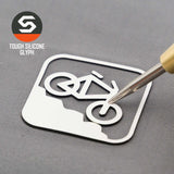 A metal tool lifts a white sticker with a mountain bike downhill icon on gray. Top left: Eternal Glyph hexagonal logo and "Mountain Bike Downhill (Silicone) - Flexfit® Mesh Trucker Cap" appear.