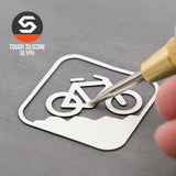 A hand uses a sculpting tool to outline the Mountain Bike Uphill (Silicone) - Flexfit® Mesh Trucker Cap by Eternal Glyph, featuring a white mountain bike trail sign on gray, with logo and “TOUGH SILICONE GLYPH” text in the top left.