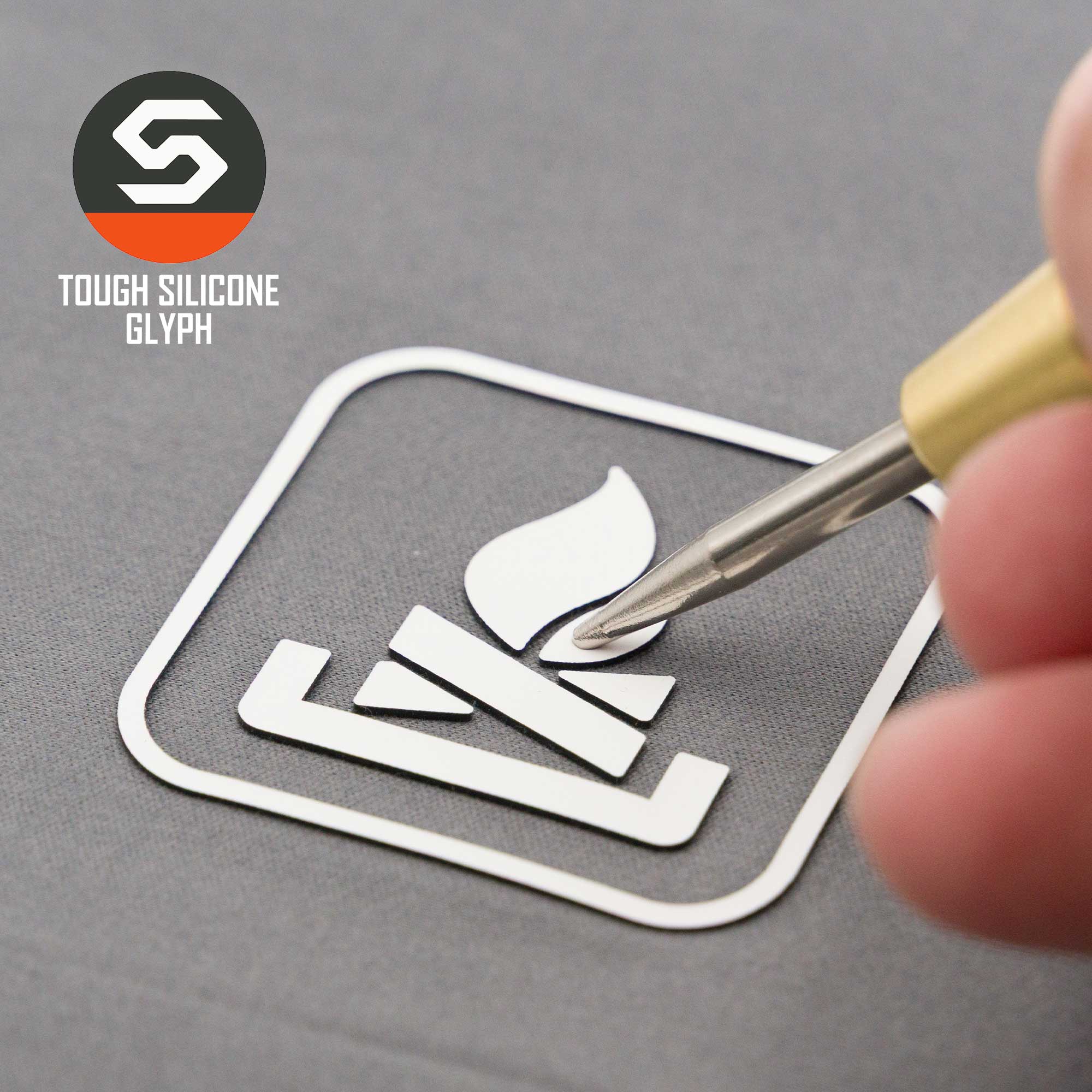 A hand uses a stylus to trace the white Campfire Trail Sign (Silicone) icon, featuring logs and flame within a square, on a gray surface. The Flexfit® Mesh Trucker Cap by Eternal Glyph is branded at the top left.