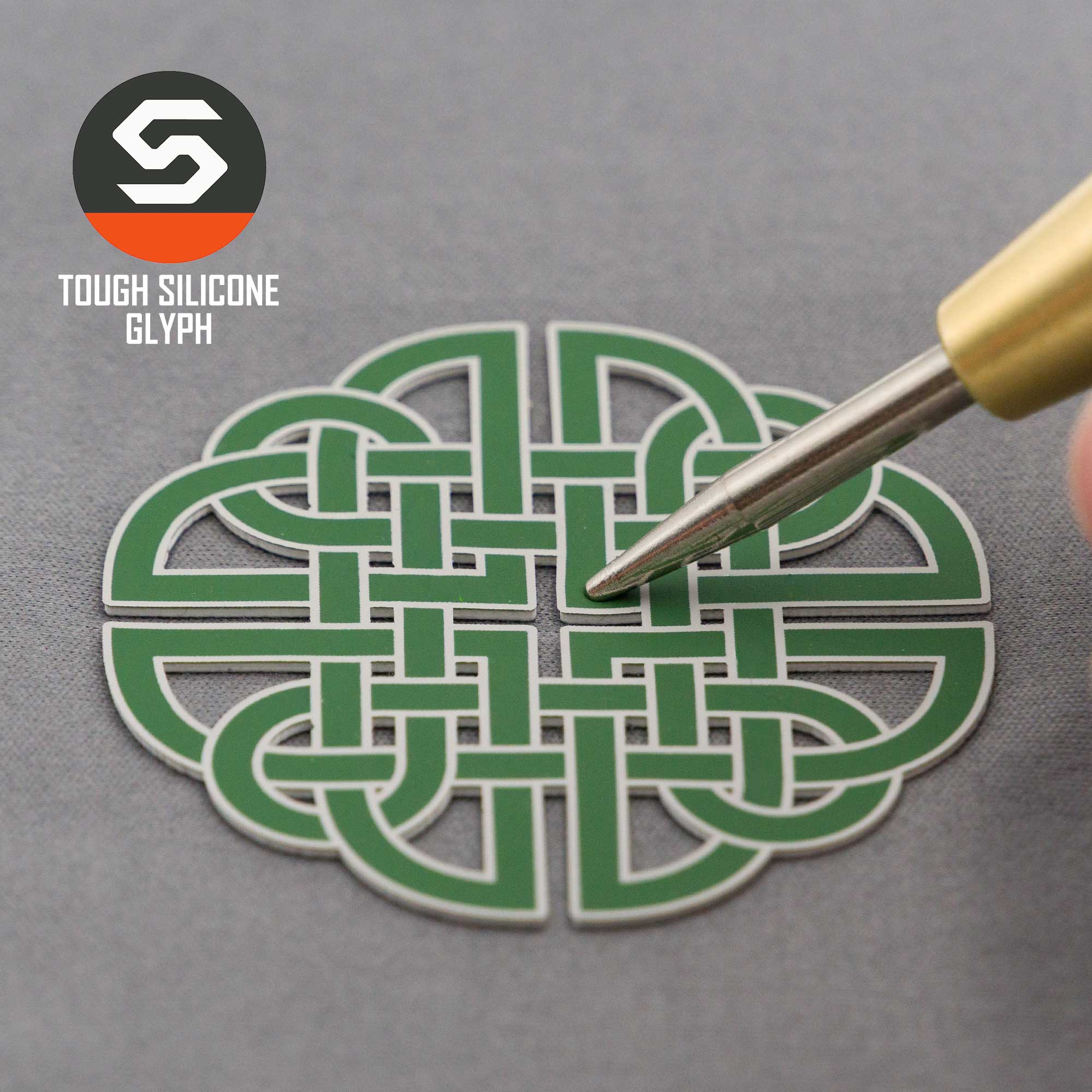 A hand holding a tool points to a green Dara Knot (Silicone) emblem on an Eternal Glyph Flexfit® Mesh Trucker Cap. The cap features "TOUGH SILICONE GLYPH" and the logo in the top left corner on a gray background.