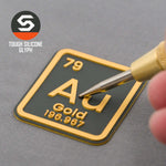 A close-up of the Eternal Glyph Gold Element (Double Layer Silicone) Flexfit® Mesh Trucker Cap shows a hand-held tool touching the gold and black patch, with “TOUGH SILICONE GLYPH” in the corner.