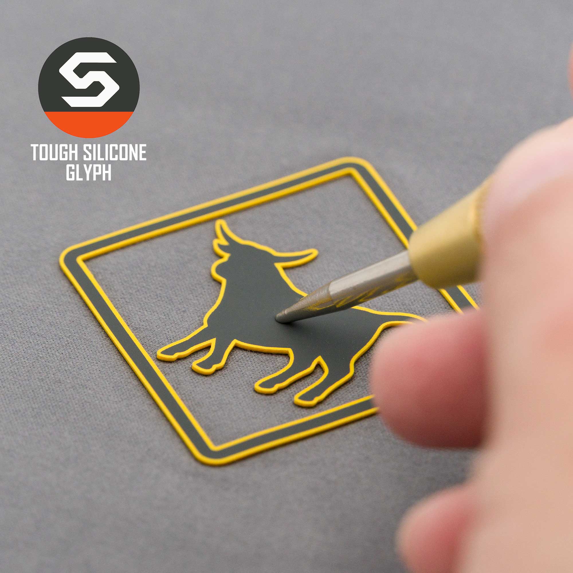 A hand applies an Eternal Glyph Open Range Sign (Silicone) sticker of a howling wolf—symbolizing untamed freedom—inside a square frame. "Tough Silicone Glyph" appears at the top left above the stylized S logo.