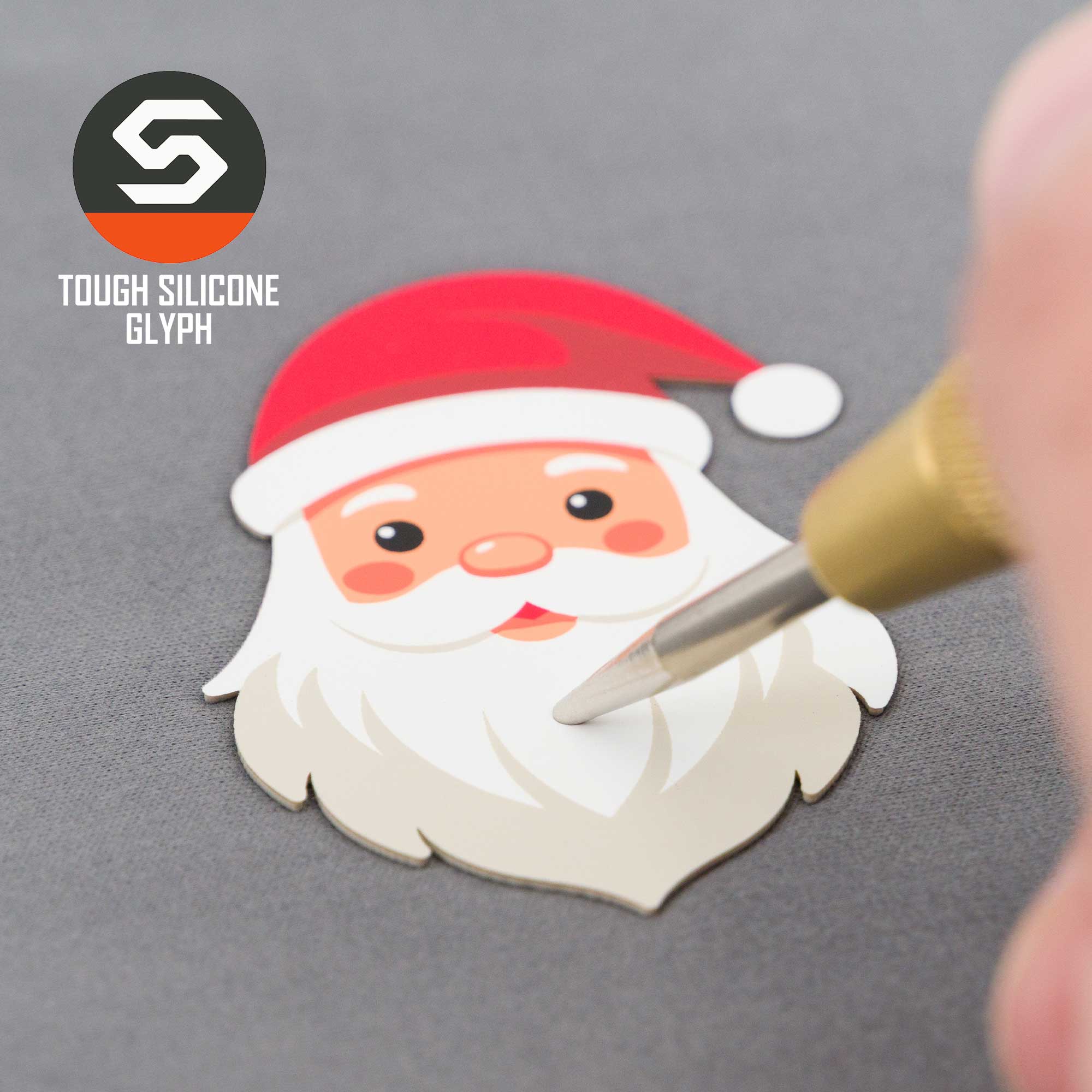 A hand traces a cute Santa Claus sticker on a Flexfit® Mesh Trucker Cap, with "TOUGH SILICONE GLYPH" and Eternal Glyph logo displayed in the top left corner.