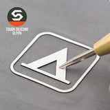 A metallic pen tip touches a white geometric glyph inside a square on gray, evoking a camping trail sign. The top left shows the Eternal Glyph logo and “Tent Camping Trail Sign (Silicone) - Flexfit® Mesh Trucker Cap.”.