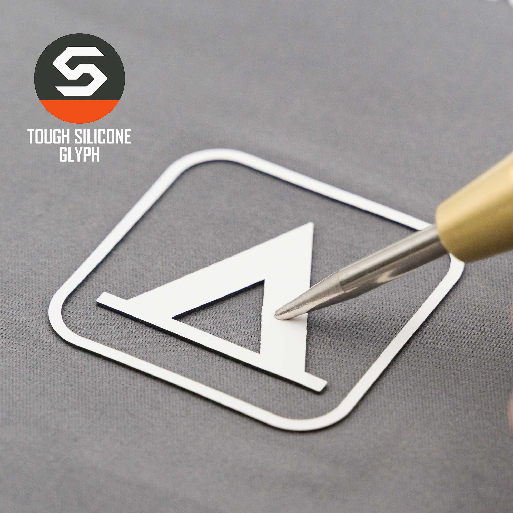 A metallic pen tip touches a white geometric glyph inside a square on gray, evoking a camping trail sign. The top left shows the Eternal Glyph logo and “Tent Camping Trail Sign (Silicone) - Flexfit® Mesh Trucker Cap.”.