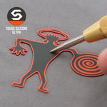 A hand holds a tool near a black and red Spiral Warrior Petroglyph (Silicone) figure with a spiral tail and wavy arms. The Eternal Glyph logo and "TOUGH SILICONE GLYPH" are shown beside a Flexfit® Mesh Trucker Cap.