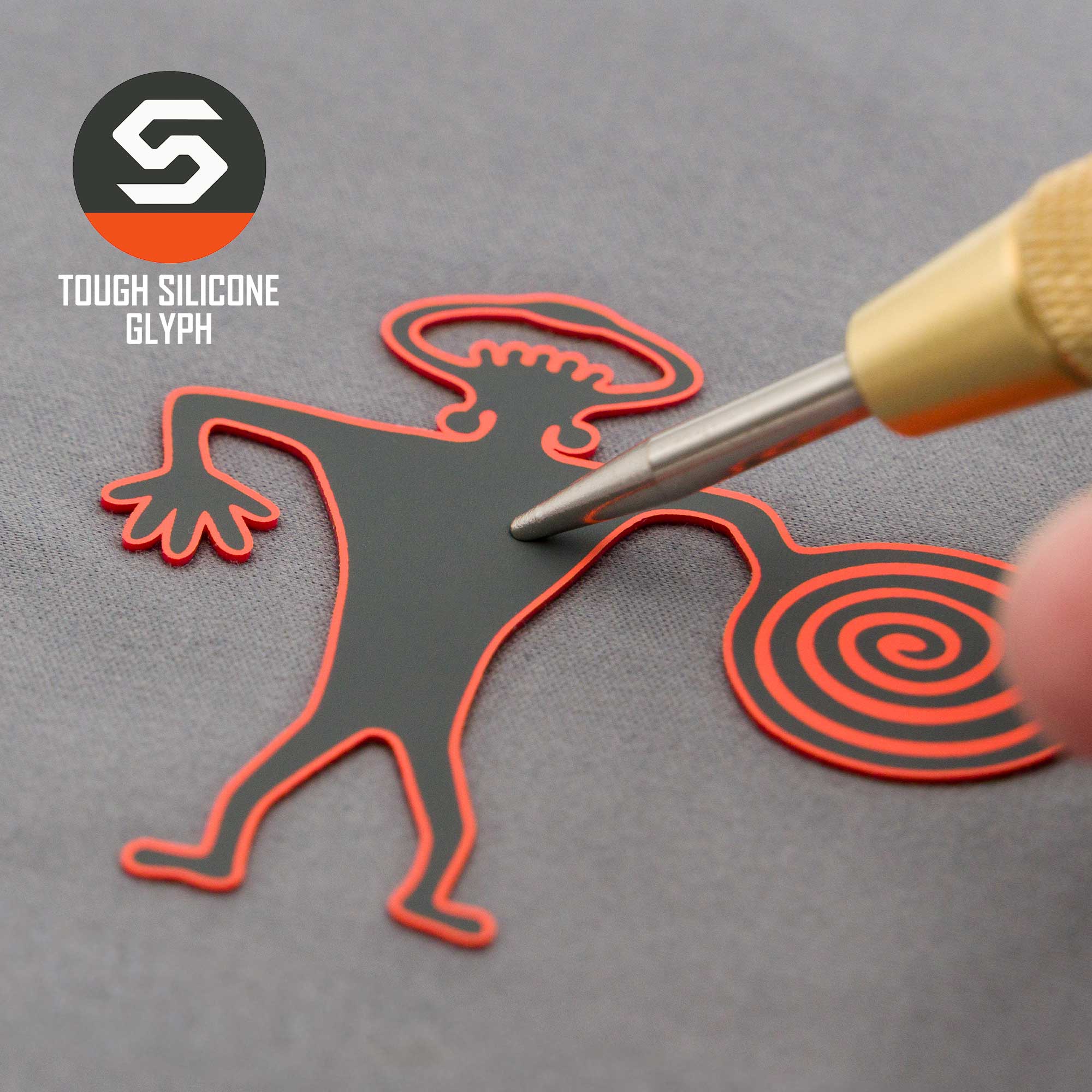 A hand holds a tool near a black and red Spiral Warrior Petroglyph (Silicone) figure with a spiral tail and wavy arms. The Eternal Glyph logo and "TOUGH SILICONE GLYPH" are shown beside a Flexfit® Mesh Trucker Cap.