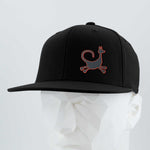 The Eternal Glyph Moab Trickster Flexfit® Flat Bill Cap features a black design with a coyote petroglyph in silicone, inspired by Moab, Utah, shown on a white geometric mannequin head against a light gray background.