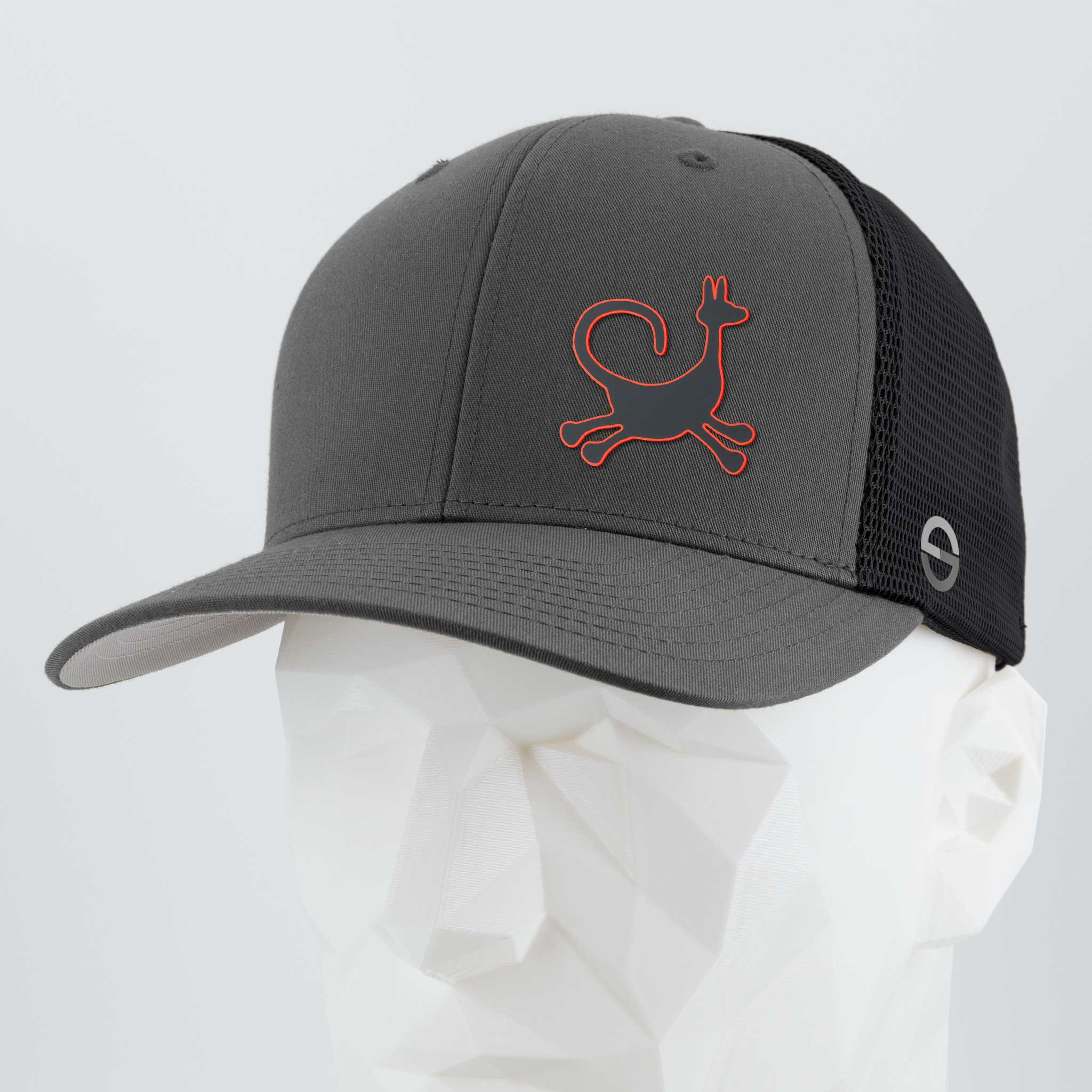 The Eternal Glyph Moab Trickster, Coyote Petroglyph Flexfit® Mesh Trucker Cap in dark gray/black features a red-outlined coyote petroglyph on the front and a small circular emblem on the side, shown on a white geometric mannequin.