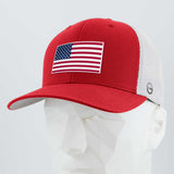 The Eternal Glyph American Flag Red/White Flexfit® Mesh Trucker Cap features double layer silicone, a mesh back, and an American flag patch, displayed on a white geometric mannequin head.