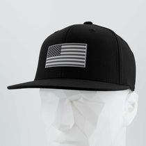 The Eternal Glyph American Flag, Monotone (Double Layer Silicone) Flexfit® Flat Bill Premium Fitted Cap in black features a grayscale flag patch and is displayed on a white geometric mannequin head against a plain light background.