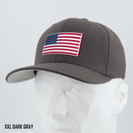 A dark gray Eternal Glyph Flexfit® Premium Wool Blend Cap, size XXL, features a red, white, and blue American flag patch on the front. Displayed on a mannequin with "XXL DARK GRAY" text at the bottom left against a light background.