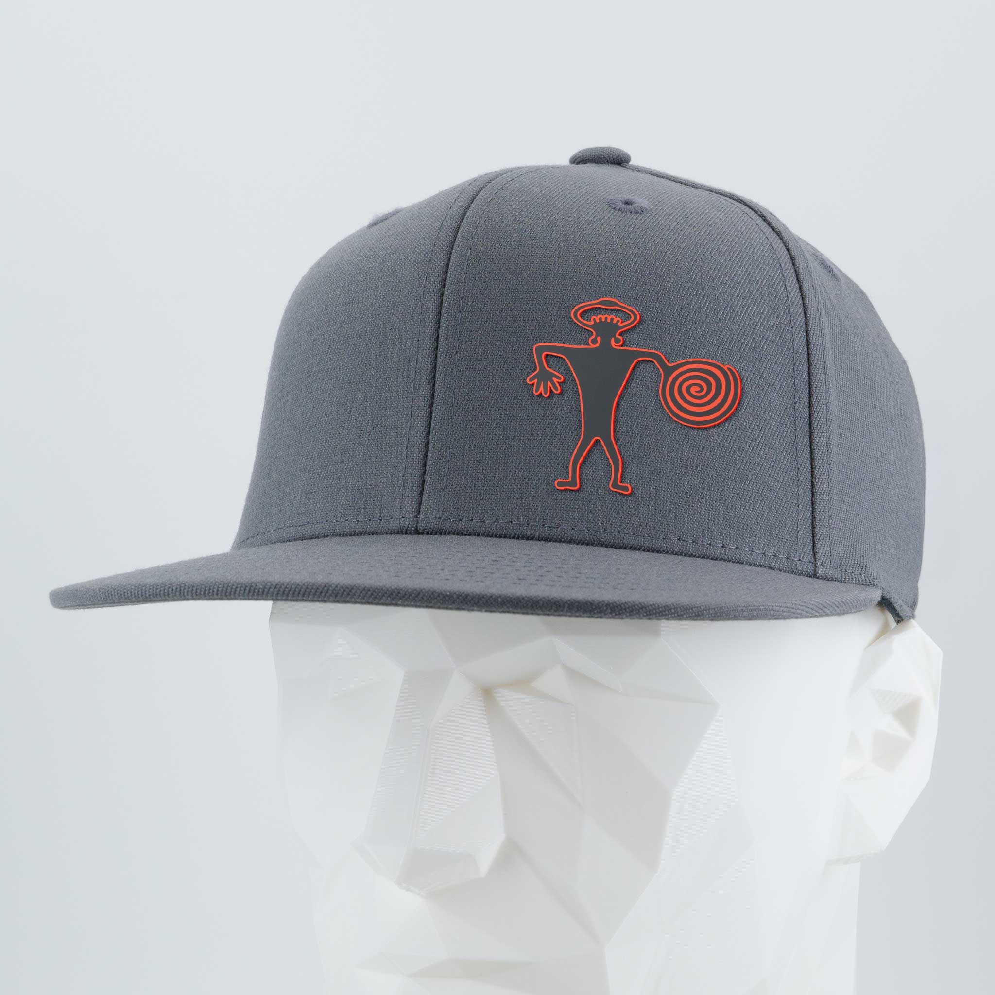 The Eternal Glyph Spiral Warrior Petroglyph (Silicone) Flexfit® Flat Bill Premium Fitted Cap features an orange Moab-inspired design on gray, shown on a white mannequin head.